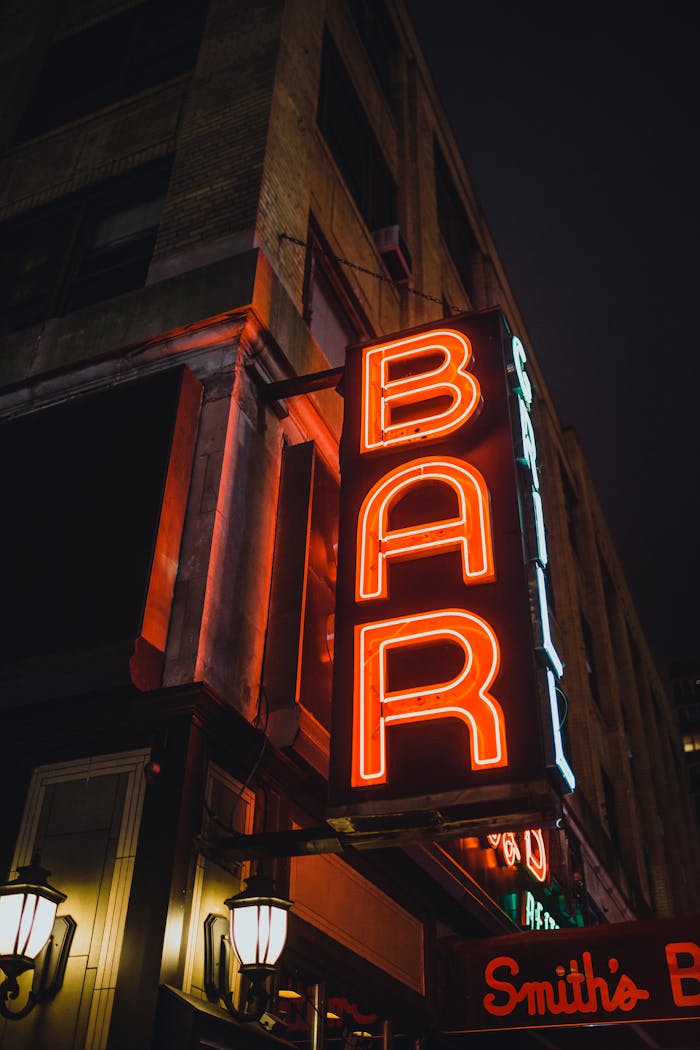 Illuminated vintage neon bar sign in an urban street at night, creating a nostalgic vibe.